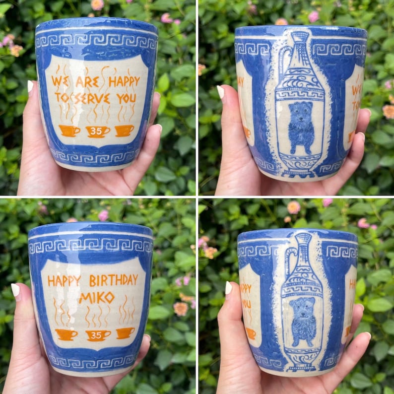 May include: A set of four ceramic mugs with a blue and white Greek key design. Two mugs feature the text "WE ARE HAPPY TO SERVE YOU" and "35" with coffee cup illustrations. The other two mugs have "HAPPY BIRTHDAY MIKO" and a dog illustration.