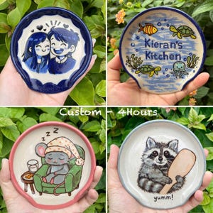 K&ouml;nnte beinhalten: Vier Keramik-L&ouml;ffelablagen mit einzigartigen Designs. Eine zeigt ein Paar, eine andere hat "Kieran's Kitchen" mit Meeresbewohnern, eine dritte zeigt eine schlafende Maus und die letzte einen Waschb&auml;ren mit einem L&ouml;ffel. Der Text "Custom - 4 Hours" ist ebenfalls sichtbar.