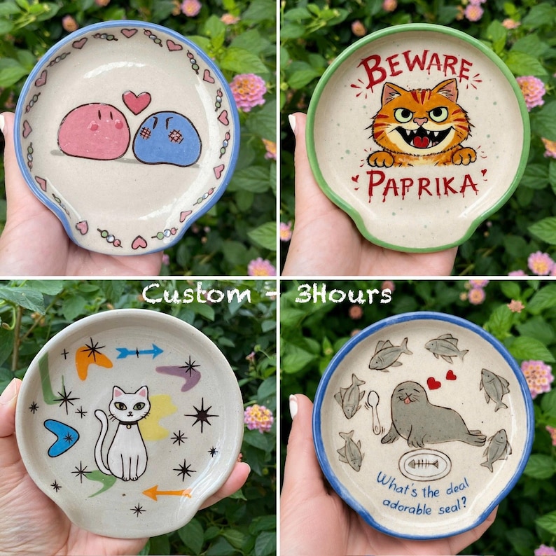 K&ouml;nnte beinhalten: Vier Keramik-L&ouml;ffelablagen mit einzigartigen Designs. Eine zeigt zwei Cartoon-Blobs mit Herzen, eine andere eine Katze mit dem Text "Beware Paprika", eine dritte eine Katze mit Retro-Formen und die letzte einen Seehund mit Fischen.