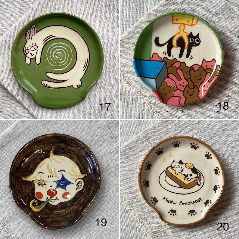 K&ouml;nnte beinhalten: Vier Keramikplatten mit einzigartigen Designs. Eine zeigt ein wei&szlig;es Kaninchen auf gr&uuml;nem Grund, eine andere schwarze Katzen und rosa B&auml;ren, eine dritte einen Clown und die letzte sagt "Meow Breakfast" mit einer Katze auf Toast.