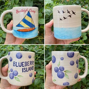May include: Four ceramic mugs with unique designs. One mug features a sailboat with the text "Burleigh Camp." Another depicts birds flying over blue water. The other two mugs have a blueberry theme, one with the text "Blueberry Island."