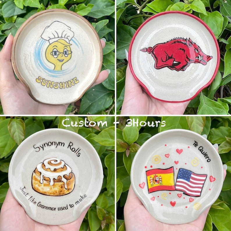 K&ouml;nnte beinhalten: Vier Keramik-L&ouml;ffelablagen mit einzigartigen Designs. Eine zeigt einen Koch mit dem Wort "Sunshine", eine andere ein rotes Wildschwein, eine dritte mit einer Zimtschnecke und dem Text "Synonym Rolls" und die letzte mit Flaggen und den Worten "Te Quiero".