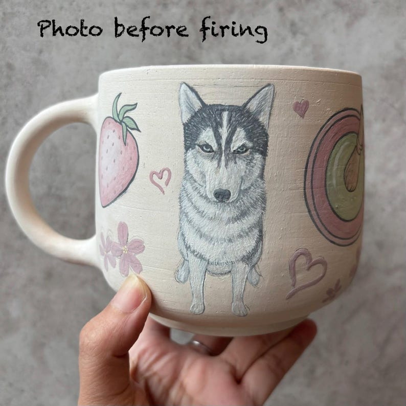 May include: A beige ceramic mug with a large handle, featuring a hand-drawn husky dog illustration. The mug is decorated with a strawberry, flowers, hearts, and the text "Photo before firing".