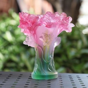May include: A pink and green glass vase with a floral design. The vase is decorated with pink flowers and green leaves.