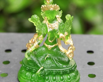 May include: Green glass statue of a deity with gold accents. The deity is sitting in a meditative pose with hands in a mudra gesture. The statue is on a green base with intricate details.