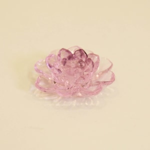 以下が含まれることがあります： 淡いピンク色の、花型の半透明なオブジェクト。 花びらは層状になっており、立体的な効果を生み出しています。 オブジェクトはおそらくガラスまたはクリスタル製で、薄いベージュ色の表面に置かれています。