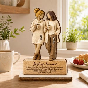 May include: A wooden tabletop figurine featuring two figures holding mugs, with the names Olivia and Sophia printed on their clothing. The base is engraved with the text Besties Forever and a poem about friendship, set on a rectangular stand.