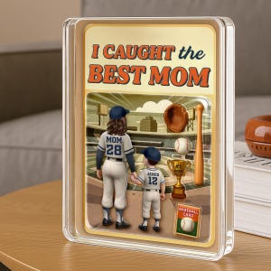 May include: A baseball-themed decorative piece with the text "I CAUGHT the BEST MOM." It features a baseball field scene with a mother and child in baseball uniforms, a baseball, bat, glove, and a trophy. The piece is encased in a clear frame.