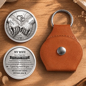 May include: Two circular silver-toned metal coins and a brown leather keychain holder. One coin features an engraving of two hands holding each other with the names Sophia and Henry. The other coin displays the text MY WIFE Never forget that I LOVE YOU.