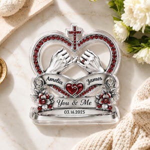 Può includere: Una targa decorativa in acrilico trasparente con una cornice a forma di cuore color argento con strass rossi, una croce in alto e due mani che si tengono per il mignolo. Include i nomi Amelia e James, il testo You & Me e la data 03.16.2025.