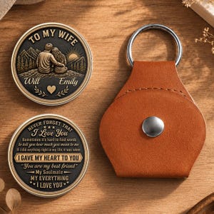 Peut inclure: Deux jetons métalliques circulaires avec des finitions noires et dorées et un porte-clés en cuir beige. Un jeton montre un couple avec des montagnes et le texte TO MY WIFE Will Emily. L'autre jeton présente du texte dont I GAVE MY HEART TO YOU.