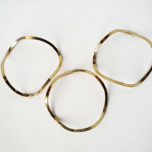 May include: Three gold-toned metal bangles with a hammered finish. The bangles are all the same shape, but different sizes.