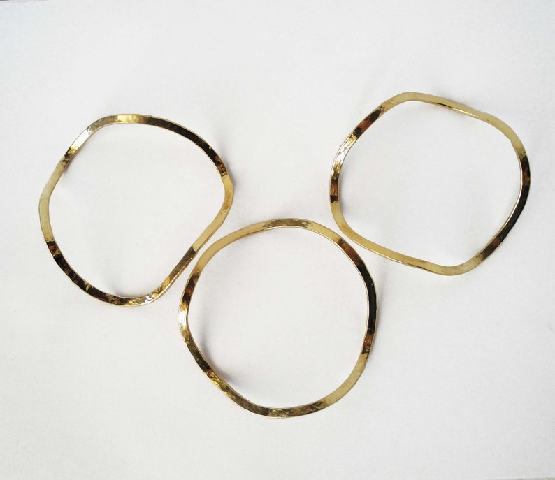 May include: Three gold-toned metal bangles with a hammered finish. The bangles are all the same shape, but different sizes.