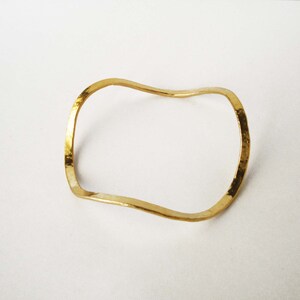 May include: A gold-toned, wavy, open bangle bracelet.