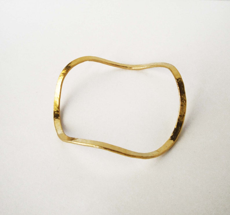 May include: A gold-toned, wavy, open bangle bracelet.