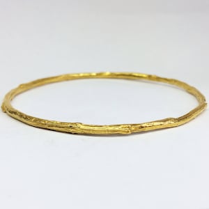 Può includere: Un braccialetto rigido in oro con un design testurizzato a forma di ramo.