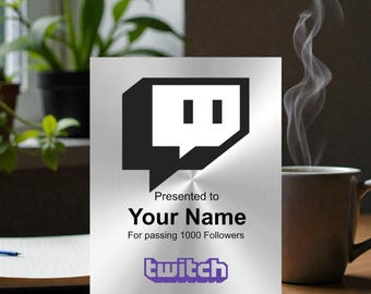 May include: A rectangular silver-toned metal plaque featuring the black Twitch logo at the top. The text reads: Presented to Your Name For passing 1000 Followers, with the purple Twitch wordmark logo printed at the bottom of the surface.