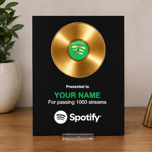 Può includere: Una targa rettangolare nera con un disco in vinile dorato nella parte superiore. Il centro del disco è verde con il testo Your Name e il logo Spotify. Sotto il disco, il testo recita Presented to YOUR NAME For passing 1000 streams.