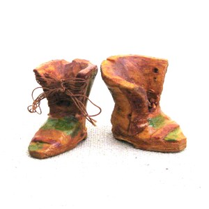 May include: A pair of brown ceramic boots with green accents and a brown string tied around the top of each boot.