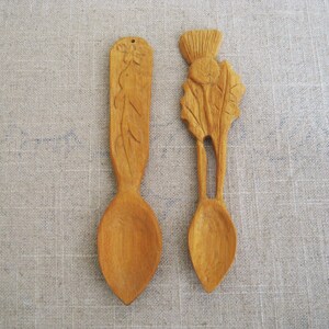 Peut inclure: Deux cuill&egrave;res en bois avec des motifs sculpt&eacute;s. Une cuill&egrave;re pr&eacute;sente un motif floral, tandis que l'autre a un chardon sculpt&eacute;.