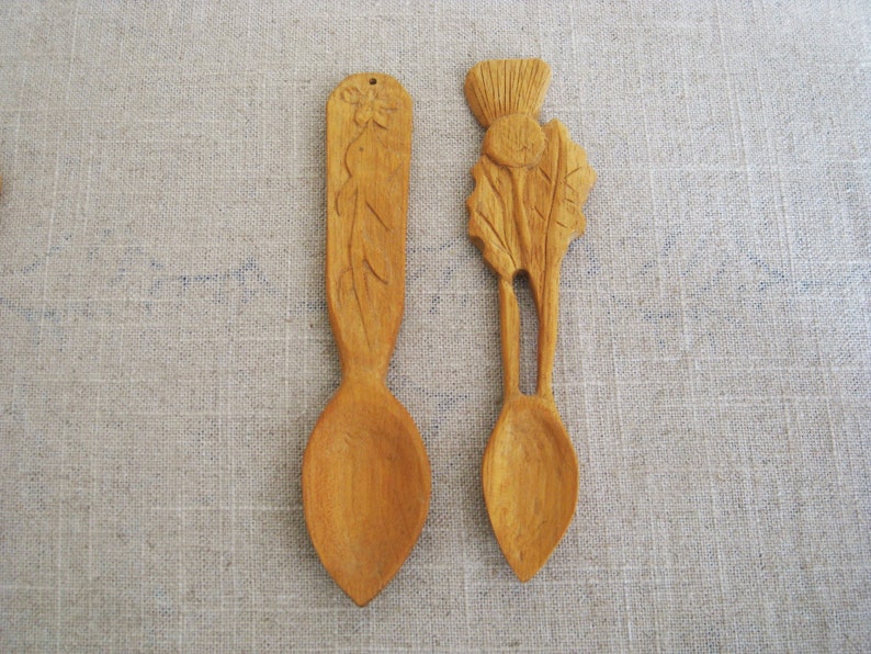 Peut inclure: Deux cuill&egrave;res en bois avec des motifs sculpt&eacute;s. Une cuill&egrave;re pr&eacute;sente un motif floral, tandis que l'autre a un chardon sculpt&eacute;.