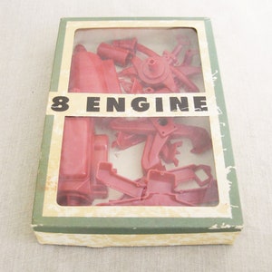 May include: A vintage model kit box with a clear plastic window showing red plastic parts for an 8 engine. The box is labeled "8 ENGINE" in black letters on a white background.