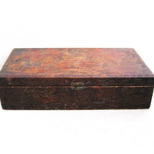 May include: A rectangular wooden box with a hinged lid. The box is a dark brown color with carved floral designs on the top and sides. A small metal clasp secures the lid. The box is likely used for storage or display.