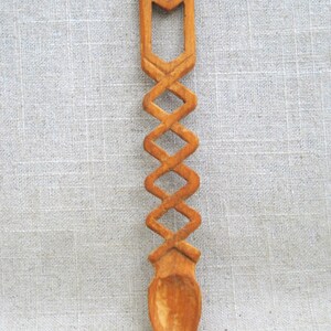 Peut inclure: Une cuill&egrave;re en bois avec un motif sculpt&eacute;. La cuill&egrave;re est brune et a un long manche avec un motif d&eacute;coratif. Le bol de la cuill&egrave;re est arrondi et lisse.
