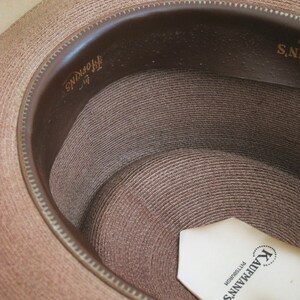 Pu&ograve; includere: Un cappello di paglia marrone con una fascia in pelle marrone e un'etichetta bianca all'interno che recita "Kaufmann's Pittsburgh".