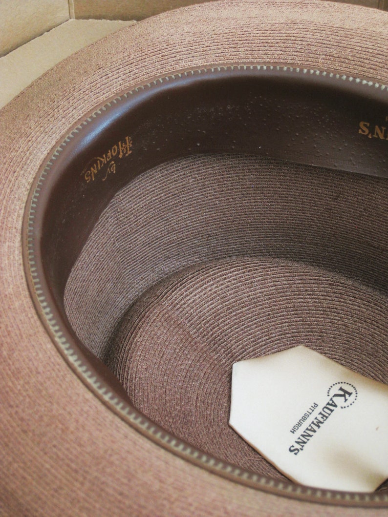 Pu&ograve; includere: Un cappello di paglia marrone con una fascia in pelle marrone e un'etichetta bianca all'interno che recita "Kaufmann's Pittsburgh".