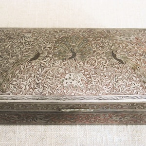 May include: A silver rectangular box with an intricate design of peacocks and floral patterns. The box has a hinged lid and a decorative latch.