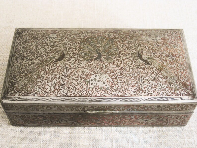 May include: A silver rectangular box with an intricate design of peacocks and floral patterns. The box has a hinged lid and a decorative latch.
