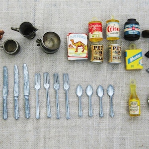May include: A collection of miniature kitchen items, including a set of silver knives, forks, and spoons, a small pitcher, a bowl, a can of condensed milk, a can of Crisco shortening, a can of coffee, a bottle of ketchup, a small iron, and a small ashtray.