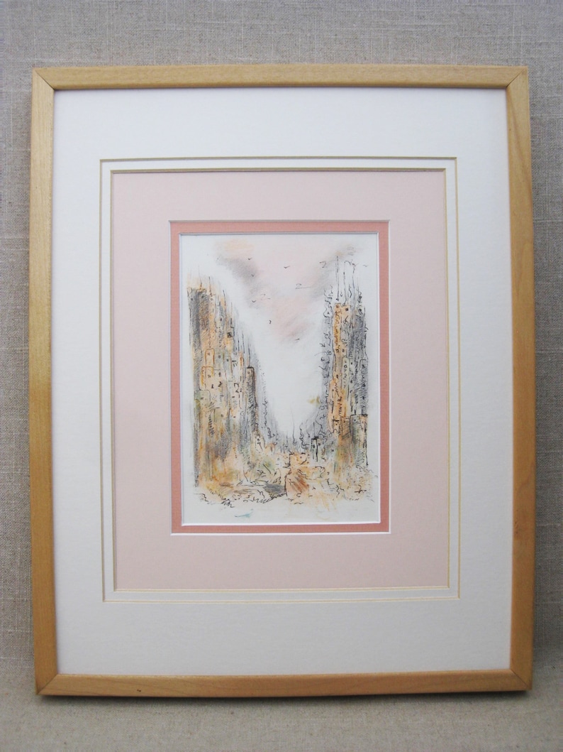 May include: A framed black and white ink drawing of a city scene with tall buildings and a pink sky. The drawing is matted in pink and white and framed in a light wood frame.
