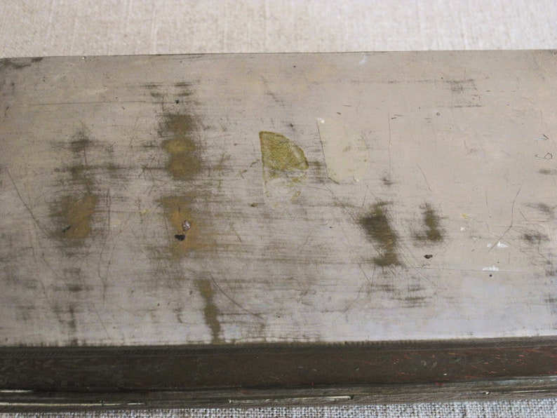 May include: A silver metal box with a worn, scratched surface. The box has a brown wooden trim around the edges.