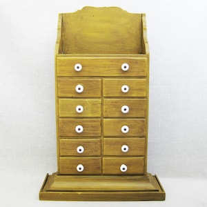 May include: A wooden cabinet with 10 drawers and white knobs. The cabinet is painted a yellow-brown color and has a decorative top.