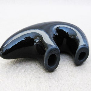 May include: A black ceramic bear figurine with a glossy finish. The bear is lying on its belly with its legs outstretched. The bear has two holes on its back.