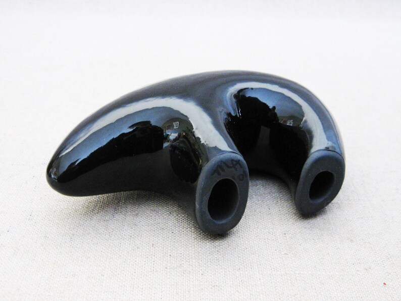 May include: A black ceramic bear figurine with a glossy finish. The bear is lying on its belly with its legs outstretched. The bear has two holes on its back.