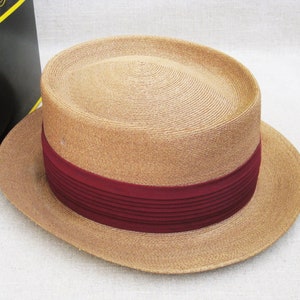 Pu&ograve; includere: Un cappello di paglia color beige con un'ampia tesa e un nastro bordeaux.