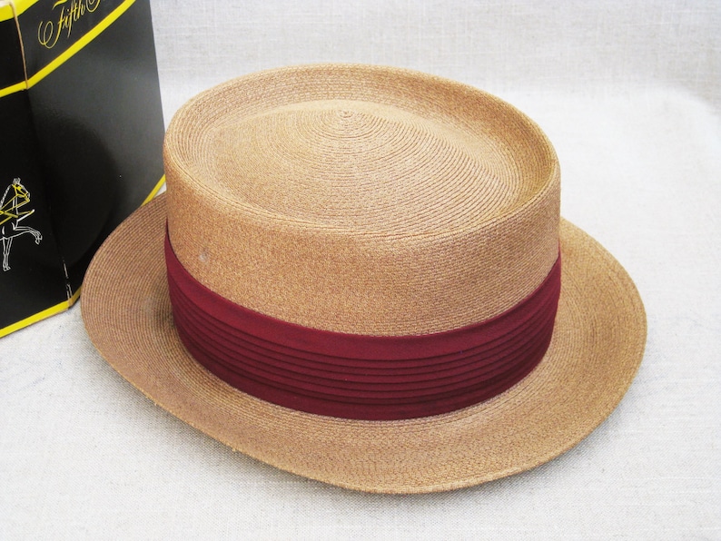 Pu&ograve; includere: Un cappello di paglia color beige con un'ampia tesa e un nastro bordeaux.