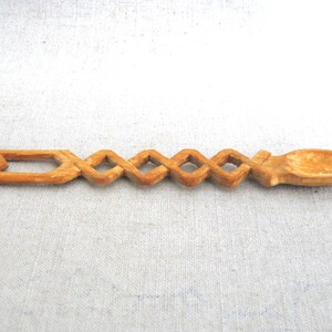 Peut inclure: Une cuill&egrave;re en bois avec un design sculpt&eacute; et complexe. La cuill&egrave;re est en bois brun clair et a un bol arrondi. Le manche est d&eacute;cor&eacute; d'une s&eacute;rie de formes de diamants.