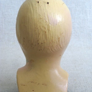 Puede incluir: Una cabeza de maniqu&iacute; de yeso vintage con un acabado agrietado de color crema. La cabeza carece de rasgos y tiene dos peque&ntilde;os agujeros en la parte superior.