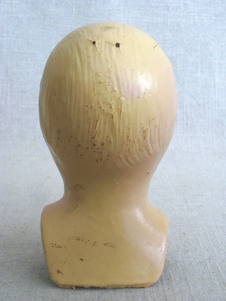 Puede incluir: Una cabeza de maniqu&iacute; de yeso vintage con un acabado agrietado de color crema. La cabeza carece de rasgos y tiene dos peque&ntilde;os agujeros en la parte superior.