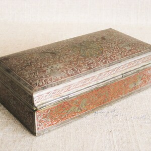 May include: A rectangular silver box with intricate floral designs and red accents. The box has a hinged lid and is decorated with a silver border.