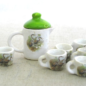 May include: A miniature tea set with a green lidded teapot and six cups. The cups and teapot are white with a brown and white bird design.