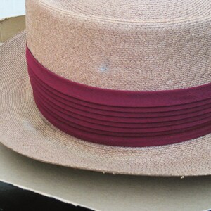 Pu&ograve; includere: Un cappello di paglia marrone con un'ampia tesa e un nastro bordeaux con pieghe orizzontali.