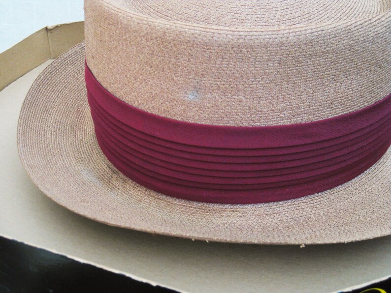 Pu&ograve; includere: Un cappello di paglia marrone con un'ampia tesa e un nastro bordeaux con pieghe orizzontali.
