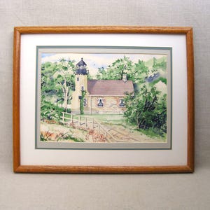 May include: A watercolor painting of a lighthouse with a small house attached. The lighthouse is white with a black roof and a green door. The house is yellow with a brown roof. The painting is framed in a wooden frame.