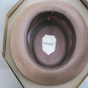 Pu&ograve; includere: Un cappello di paglia marrone con una fascia in pelle marrone e un'etichetta bianca all'interno che recita "Kaufmann's Pittsburgh".