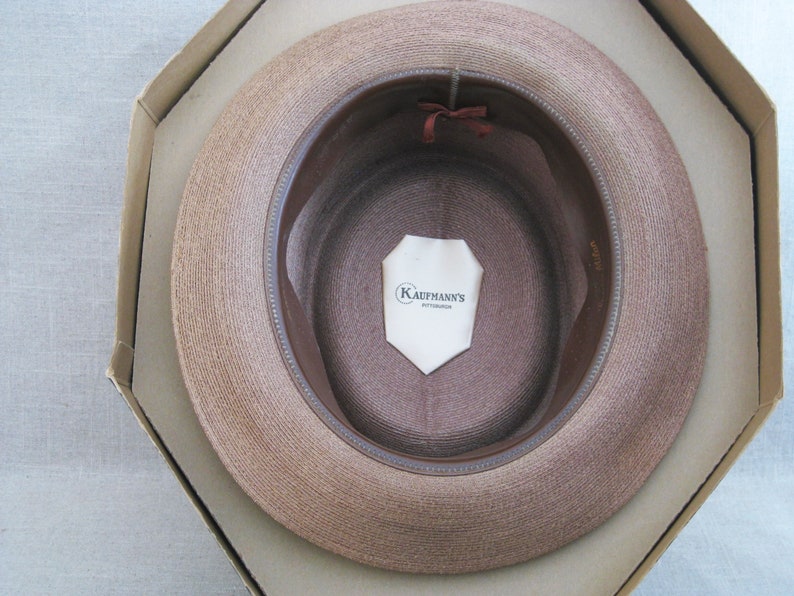 Pu&ograve; includere: Un cappello di paglia marrone con una fascia in pelle marrone e un'etichetta bianca all'interno che recita "Kaufmann's Pittsburgh".
